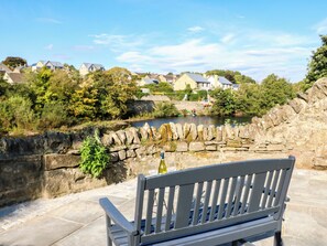 A stone wall with a bench in the foreground, overlooking a river with houses in the background. - 18 Thorngate Wynd (Barnard Castle)
