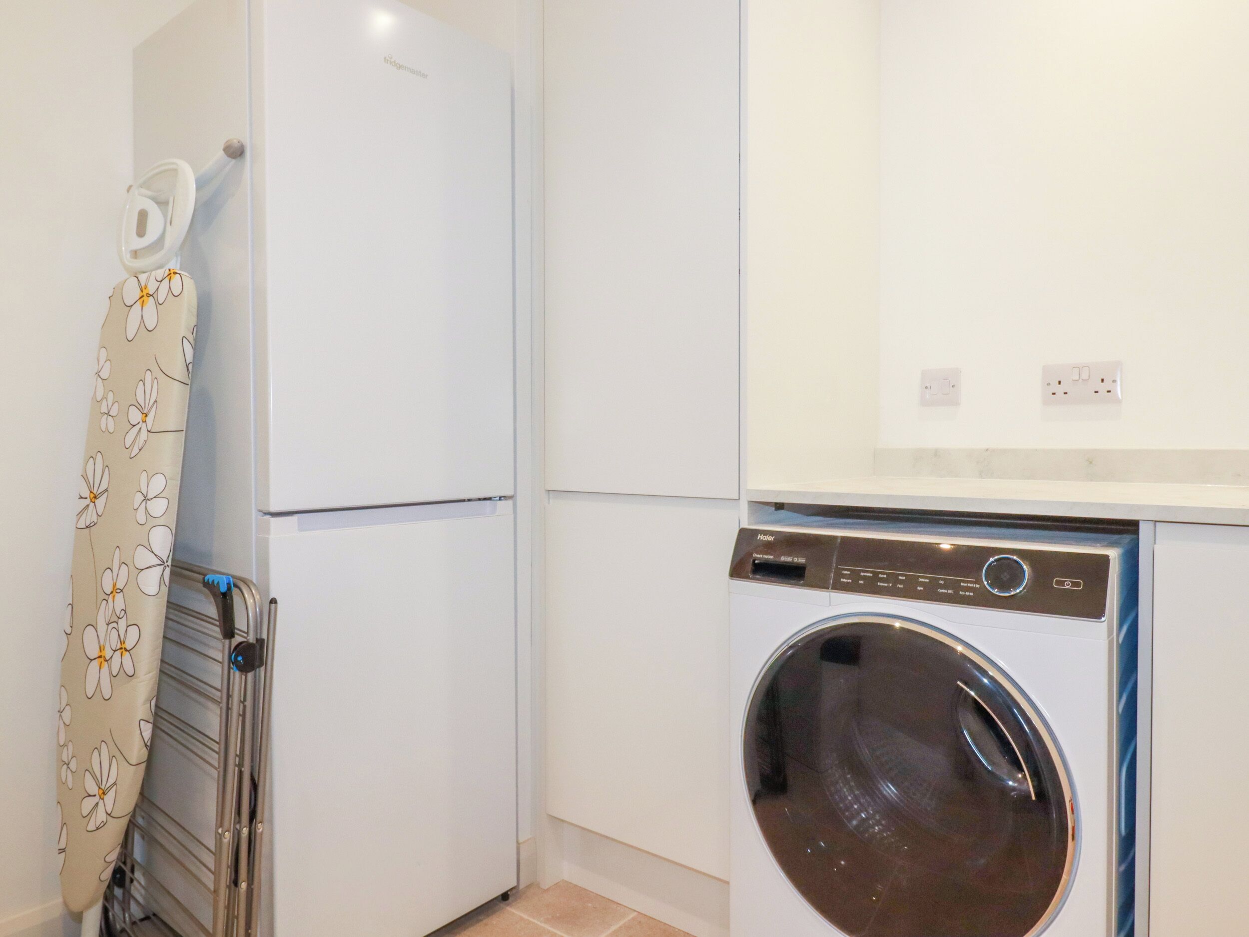 A compact laundry room with a white refrigerator, a washing machine, and a drying rack.