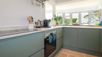 Una cucina moderna con mobili color petrolio, forno integrato e finestra con vista su un giardino.