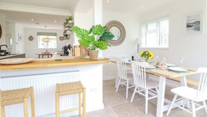 A bright kitchen with a central island, white chairs, and a dining table set for four. - Polwen (Padstow)