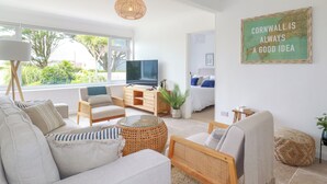A modern living room with a large window, a television, and a bed in the background. - Polwen (Padstow)