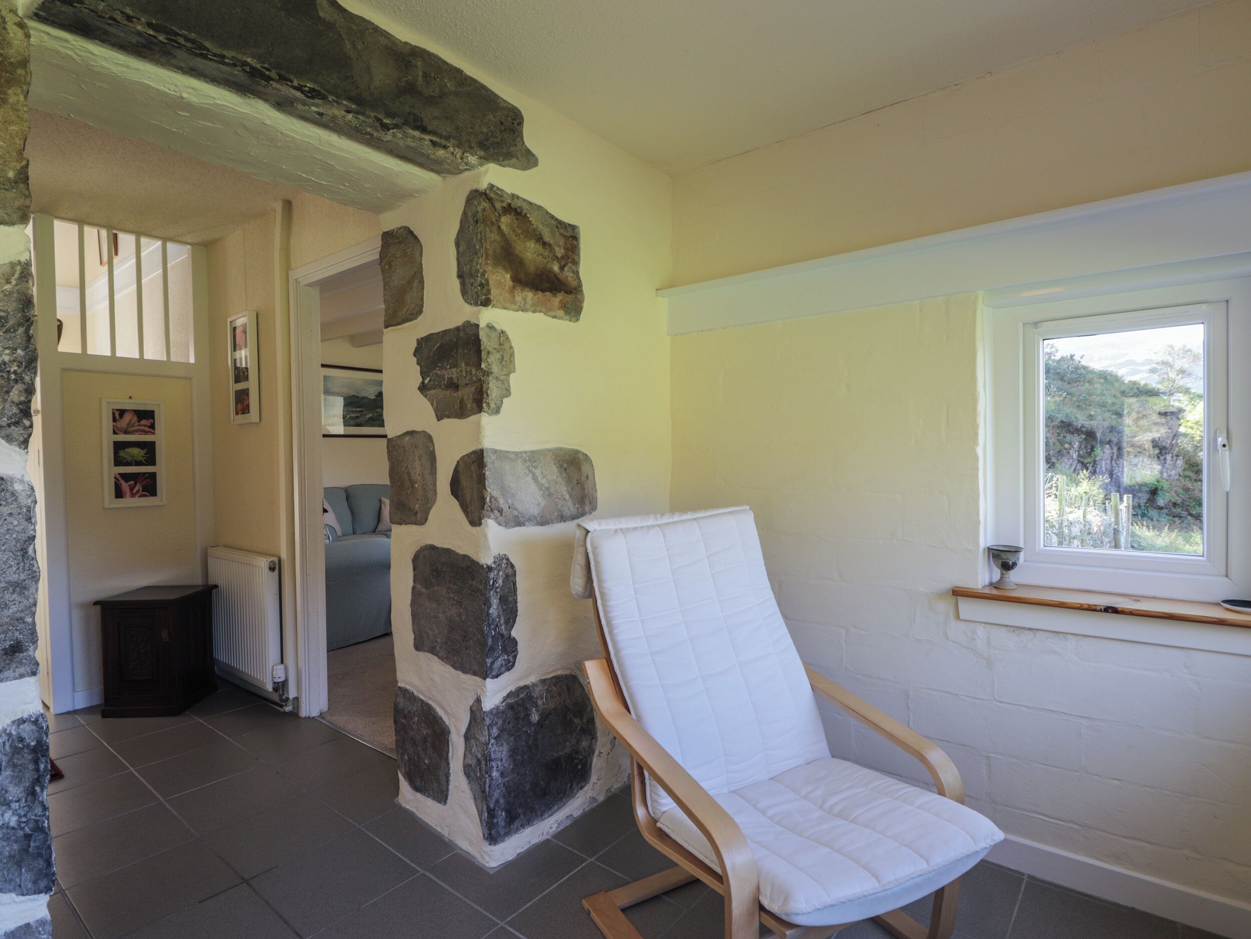 Une pièce avec un mur en pierre, une chaise en bois, une fenêtre donnant sur un paysage agréable et une porte menant à une autre pièce.