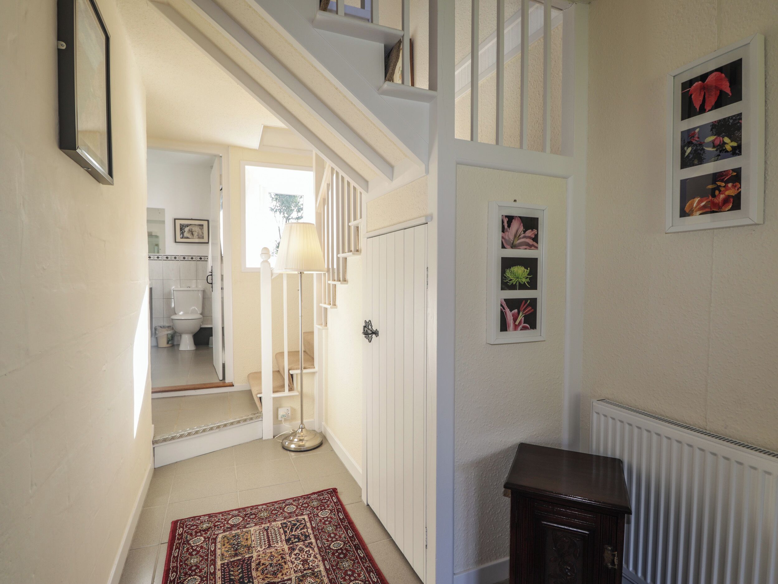 A hallway with a staircase, a radiator, and framed floral pictures on the wall.