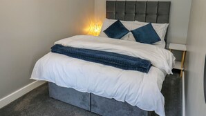 A neatly made bed with white and blue bedding, a grey headboard, and a small bedside table with a lamp. - 69 Main Street (Keighley)