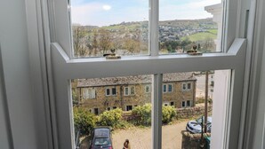 A view through a window with a clear sky, a brick building, and parked cars. - 69 Main Street (Keighley)