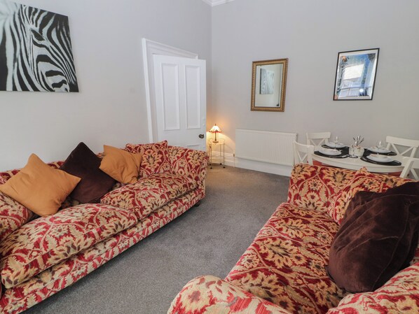 A living room with patterned sofas, a dining table set for two, and a radiator.