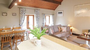 A cozy living room with a wooden ceiling, a dining area with a table set for two, and a sofa with decorative pillows. - Dove Cottage (Leek)