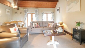 A cozy living room with a brown leather sofa, a grey sofa with colorful cushions, a wooden coffee table, and a black cabinet with a glass door. - Dove Cottage (Leek)