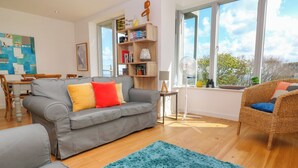 A modern living room with a grey sofa, a blue rug, and a wicker chair. - Talland View (St Ives)