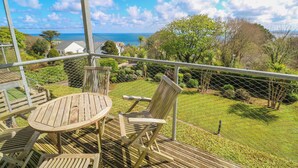 A deck with a table and chairs, overlooking a well-maintained garden and a view of the sea. - Talland View (St Ives)