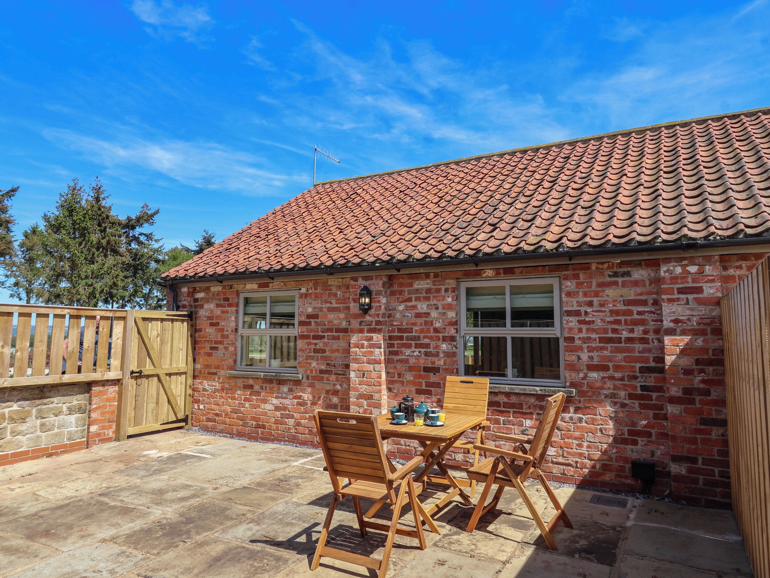 A brick house with a tiled roof, a wooden gate, and a patio with a table and chairs.