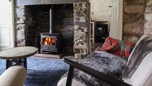 A cozy room with a stone fireplace, a sofa with a plaid blanket, and a small round table. - Nyth Yr Eryr (Blaenau Ffestiniog)