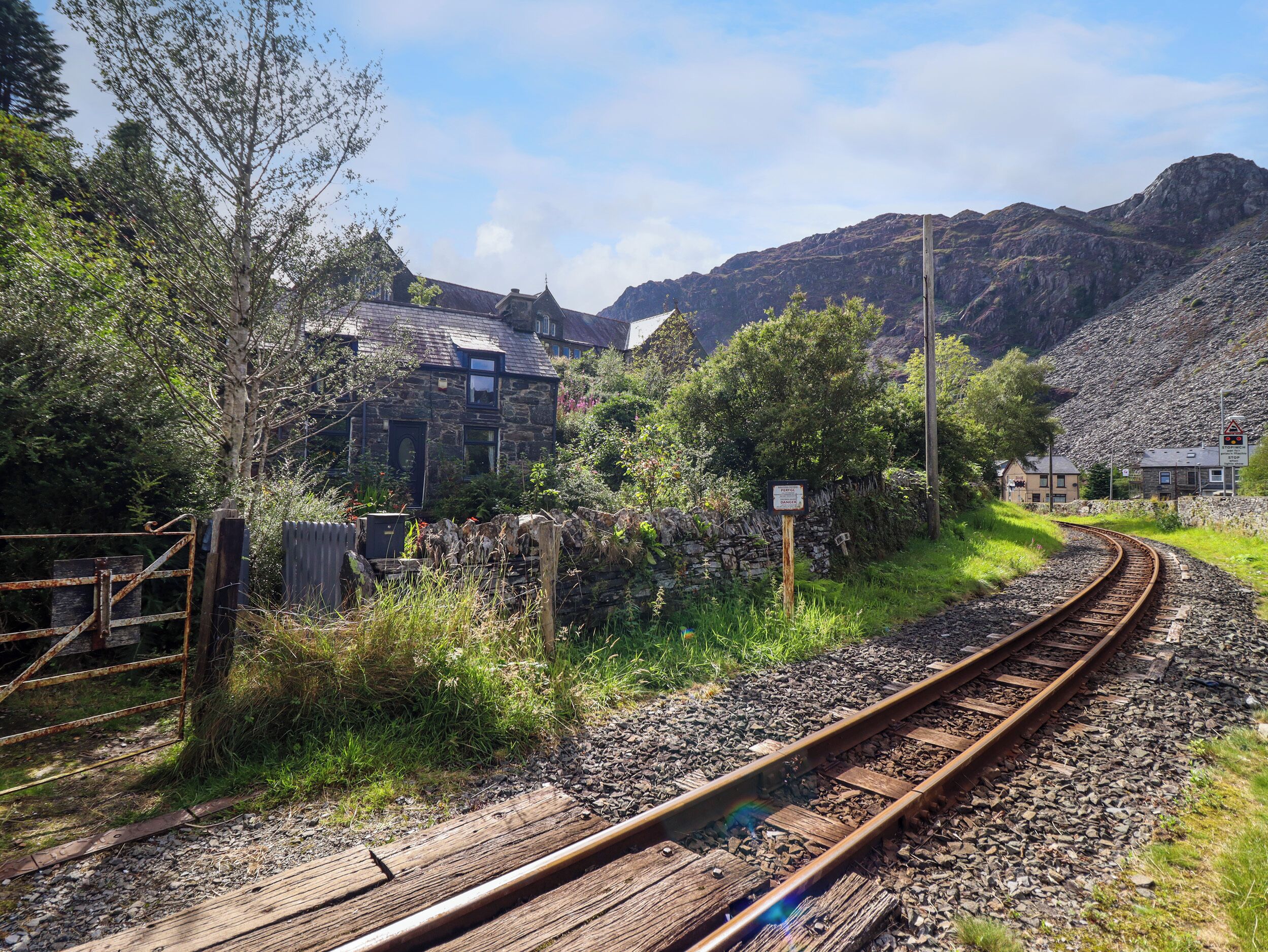 A rural railway track with a stone house and a wooden fence.