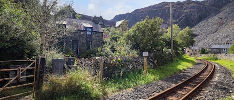 A rural railway track with a stone house and a wooden fence.