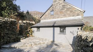 A stone house with a sloped roof, a small window, and a stone pathway leading to the entrance. - Nyth Yr Eryr (Blaenau Ffestiniog)