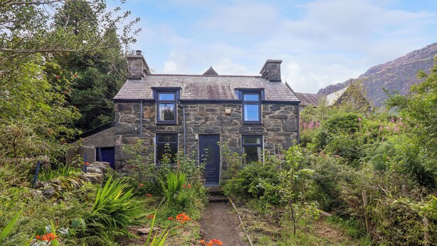 A stone house with a garden path leading to the entrance, surrounded by lush greenery and flowers. - Nyth Yr Eryr (Blaenau Ffestiniog)