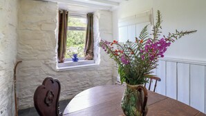 A dining area with a wooden table, a vase with flowers, and a window with curtains. - Nyth Yr Eryr (Blaenau Ffestiniog)