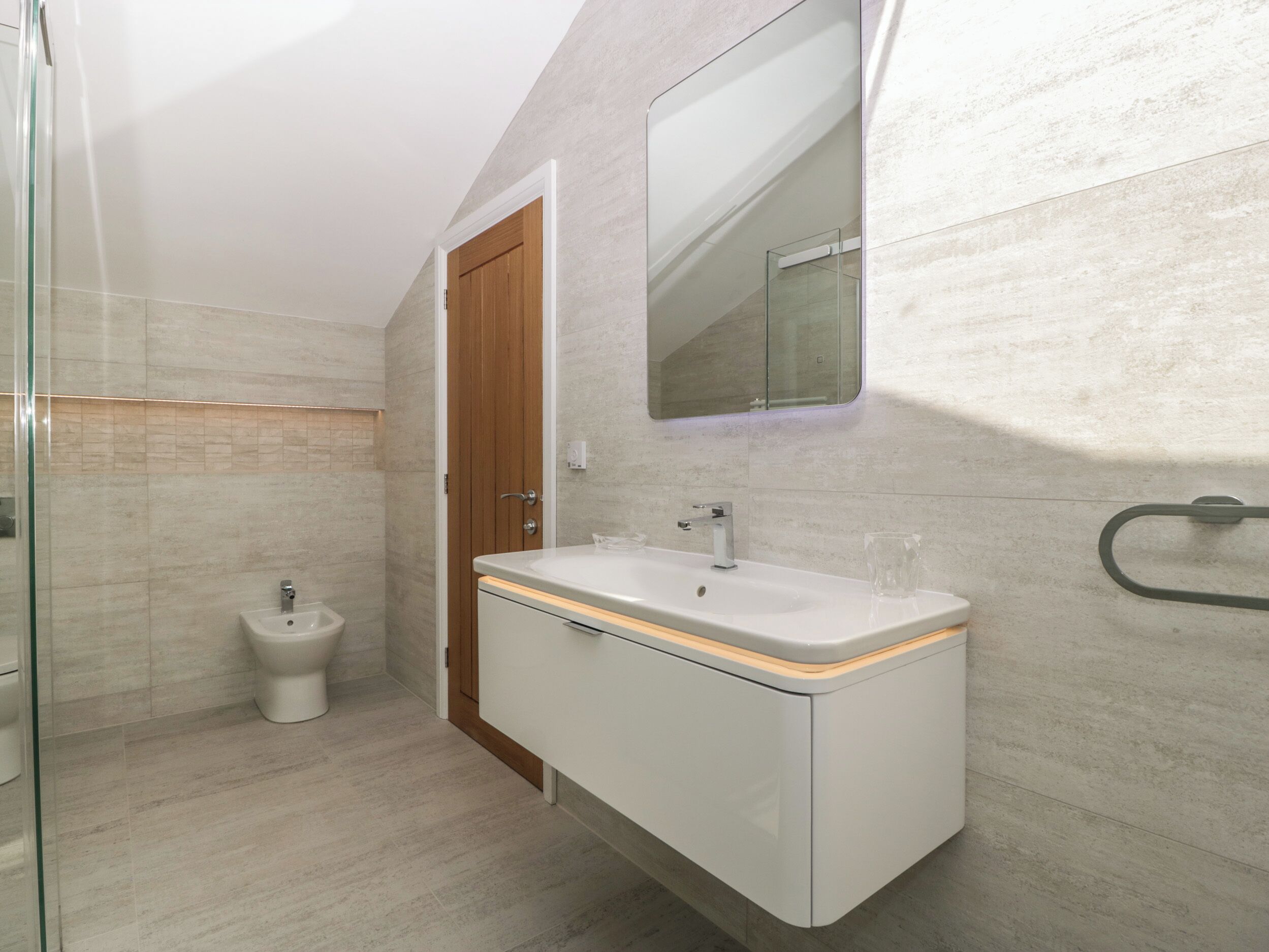 A modern bathroom with a glass shower enclosure, a white sink with a wooden countertop, and a wooden door.
