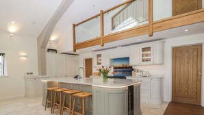 A spacious kitchen with a central island, wooden stools, and a view of the outdoors through a large window. - Hidden Well (Bristol)