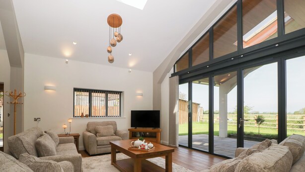 A spacious living room with a large sofa set, a wooden coffee table, and a television. There is a large sliding glass door leading to a patio with a view of the outdoors. - Hidden Well (Bristol)