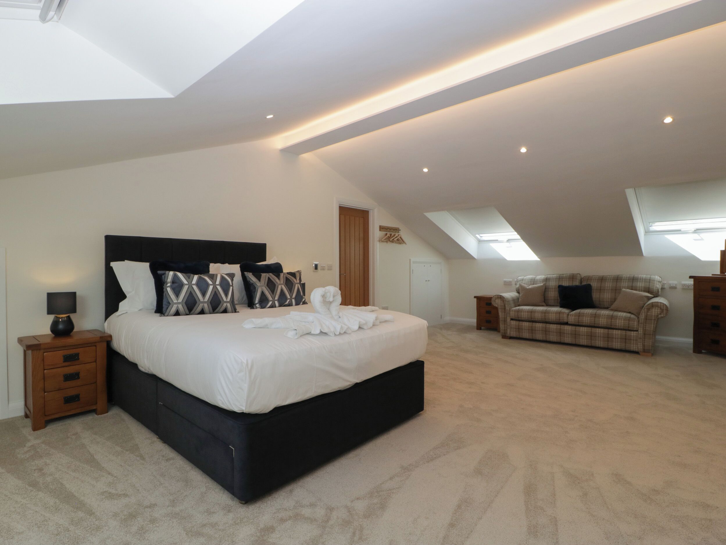 A spacious bedroom with a large bed, a sofa, and a skylight.