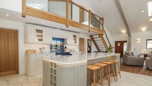 A spacious kitchen with a central island, wooden bar stools, and a staircase leading to an upper level. - Hidden Well (Bristol)