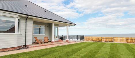 A house with a covered porch, a lawn, and a wooden fence overlooking the sea.