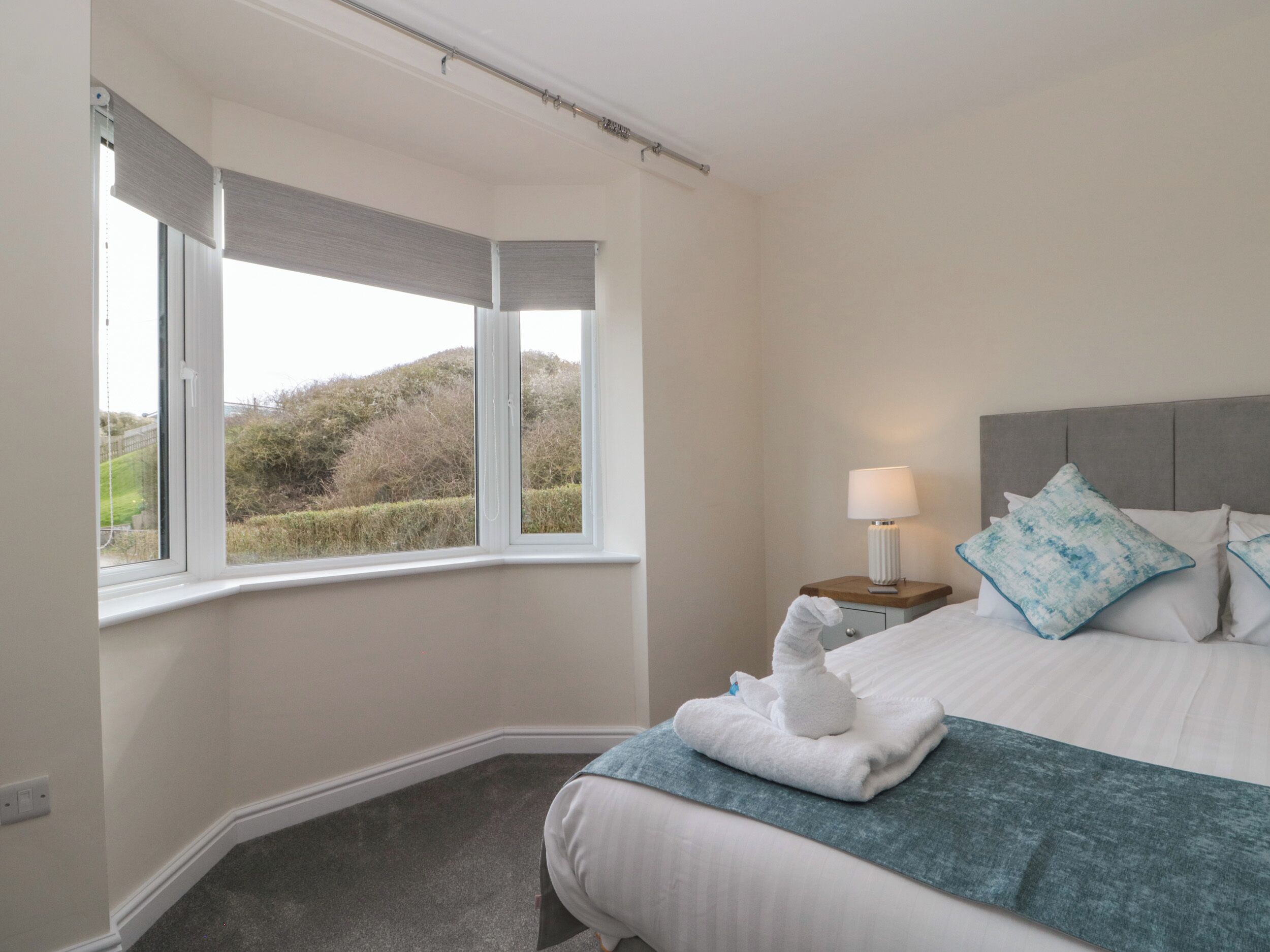 Habitación de hotel con cama, mesita de noche con lámpara y vista al exterior por la ventana.