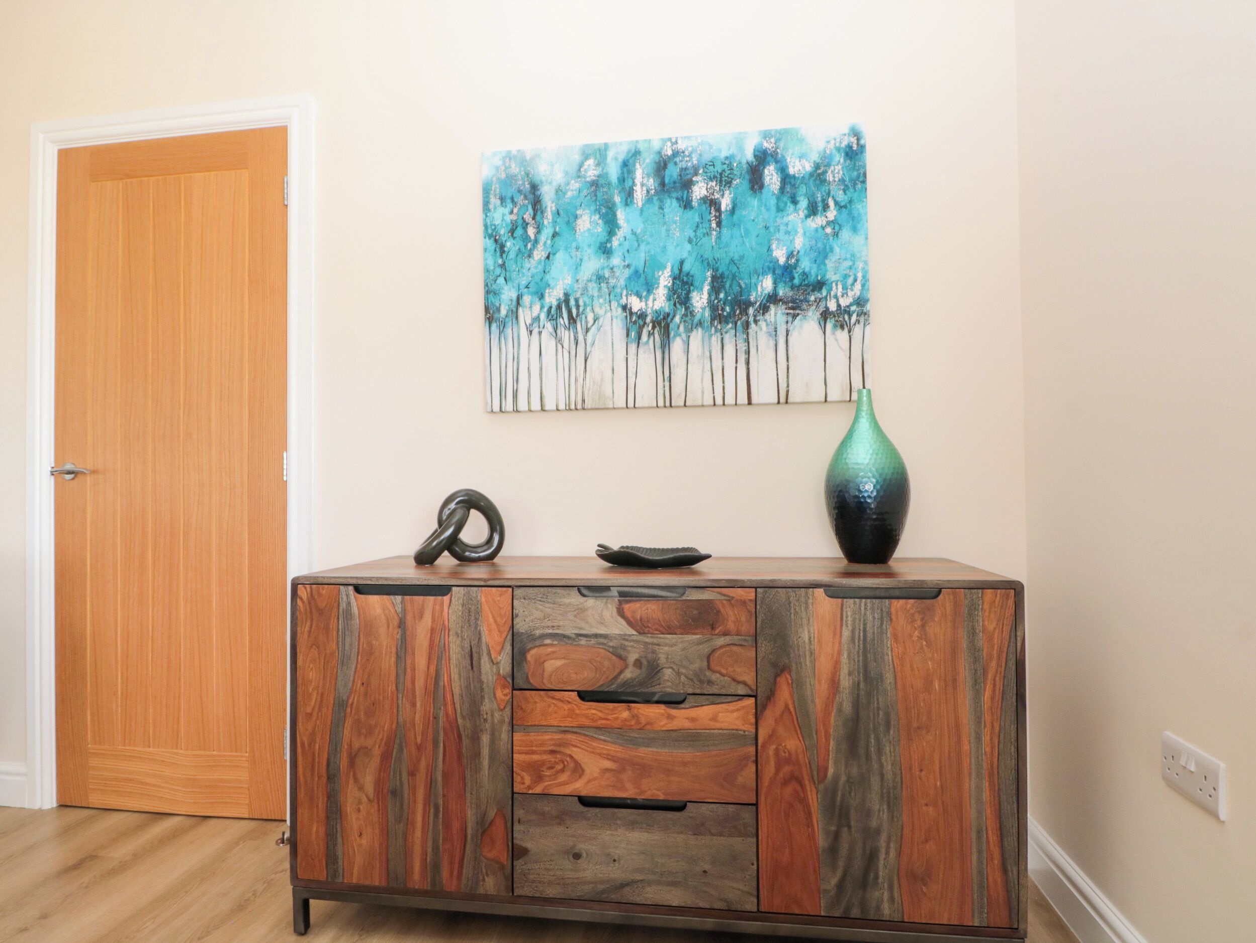 A wooden cabinet with drawers, a vase, and a painting on the wall.