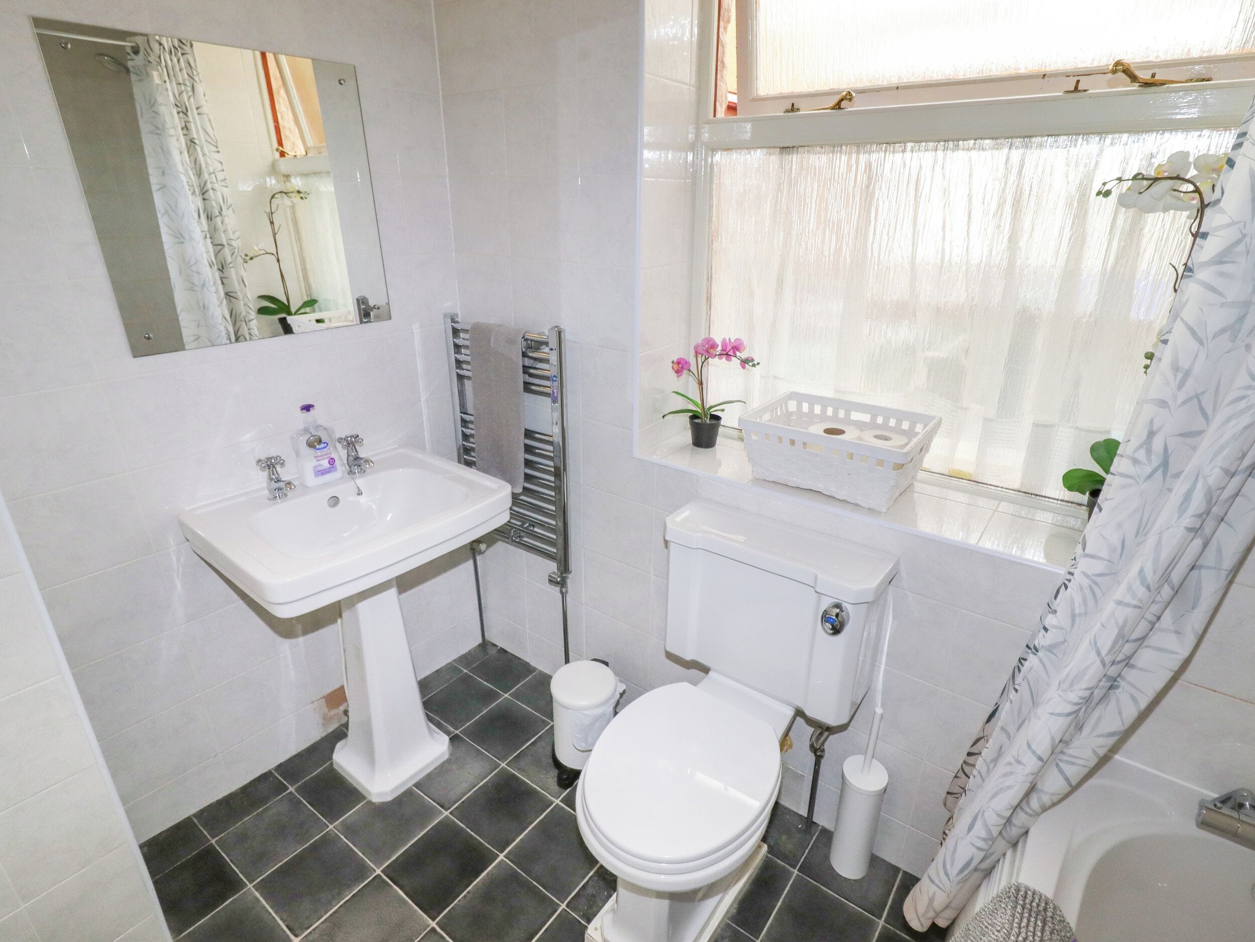 A bathroom with a white sink, toilet, and bathtub. There is a window with a curtain, a towel rack, and a small plant on the windowsill.