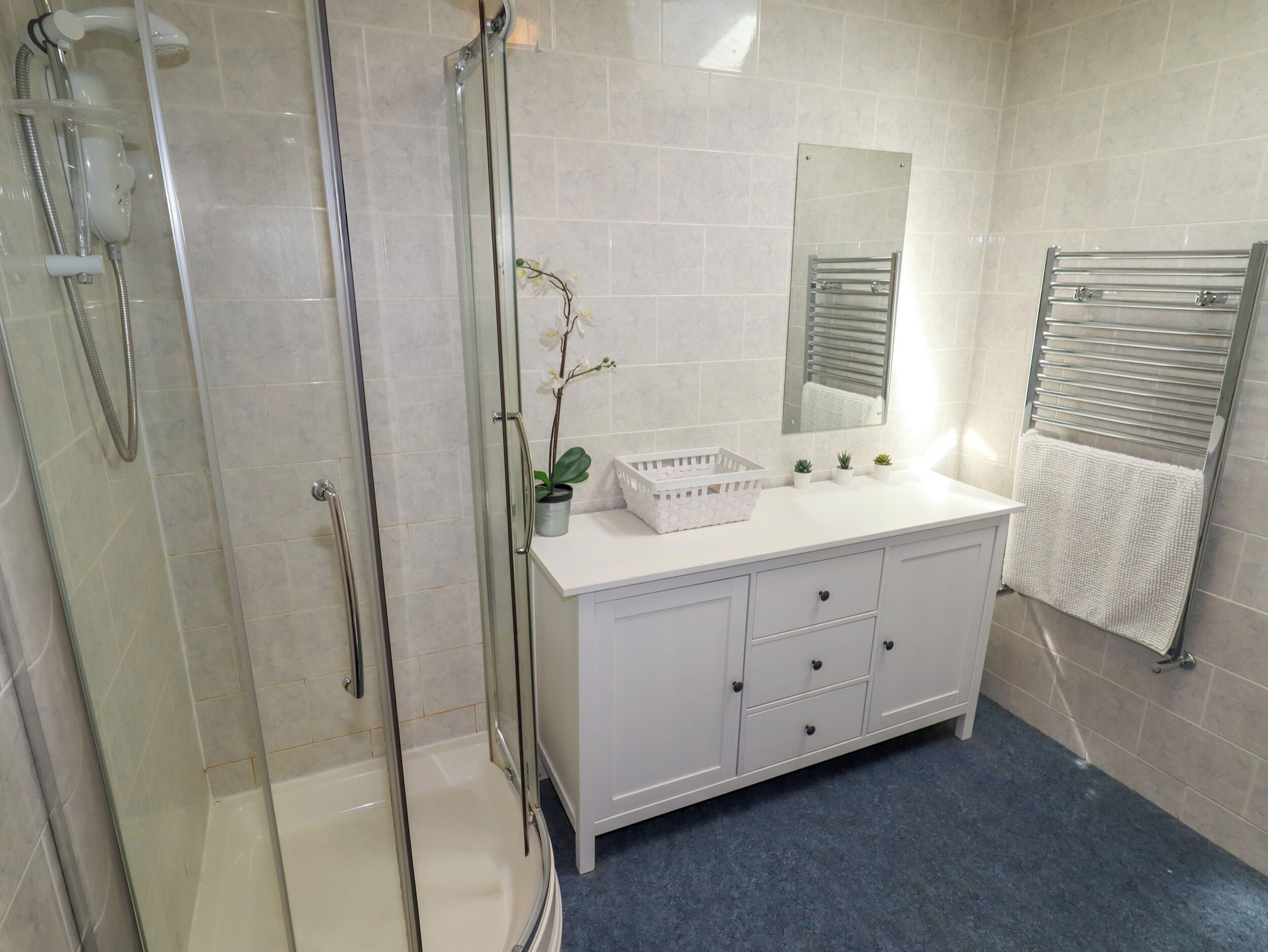 Uma casa de banho moderna com cabine de duche em vidro, toucador branco com espelho e um porta-toalhas.