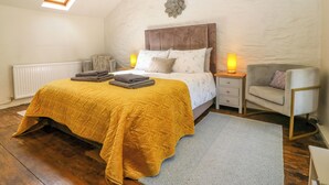 Un dormitorio con cama, lámparas de noche, una silla, un radiador y un tragaluz.