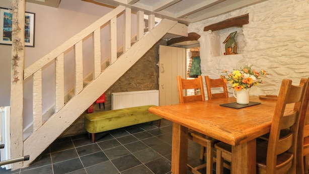 Un comedor con mesa y sillas de madera, un banco, una escalera y una pared de piedra.