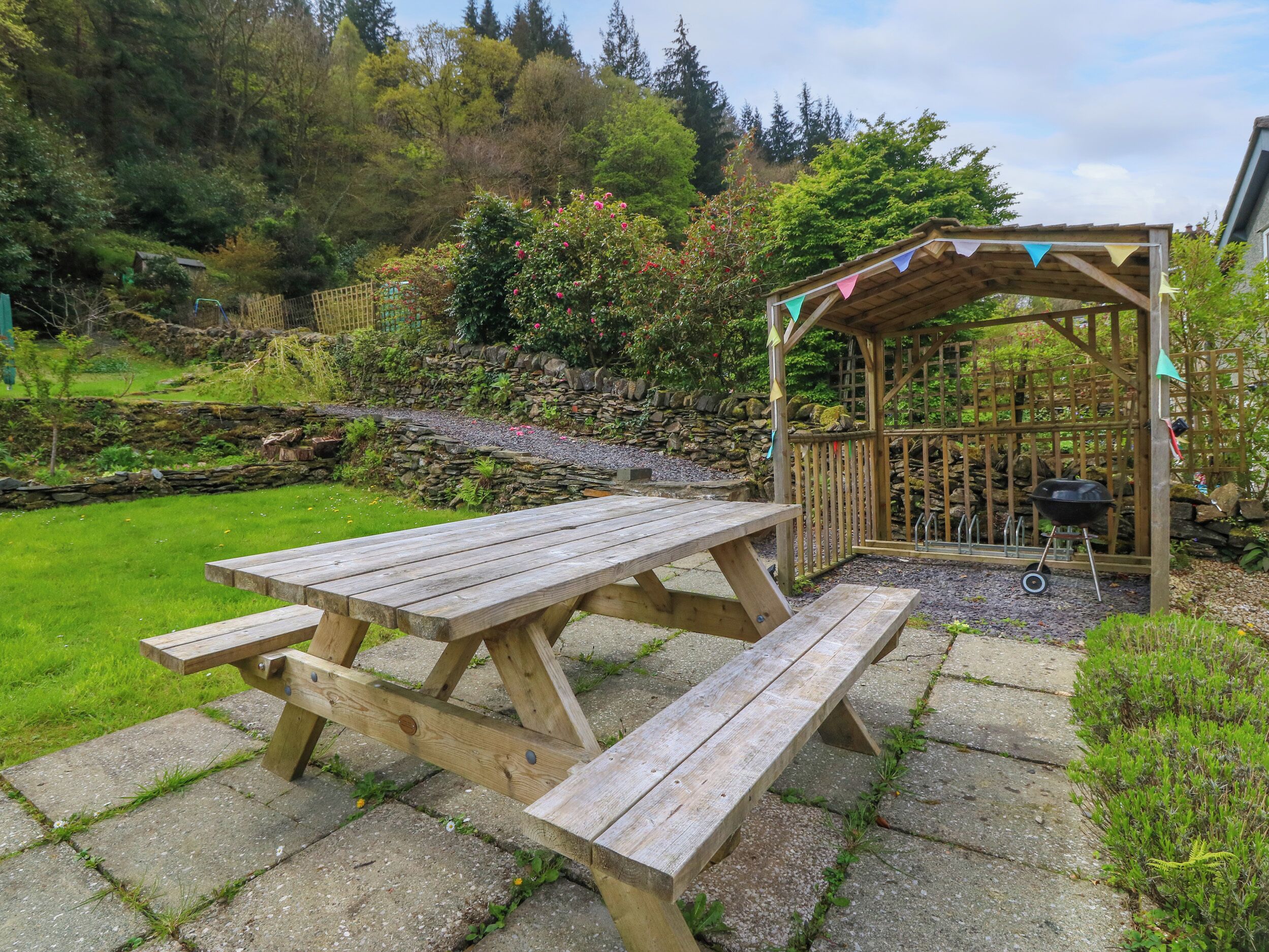 Ein Holztisch mit Bänken in einem Gartenbereich mit einer Steinmauer und einer Holzpergola.