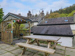A wooden gazebo with colorful flags, a barbecue grill, and a picnic table in a garden area. - 2 Banc Llugwy (Betws-Y-Coed)