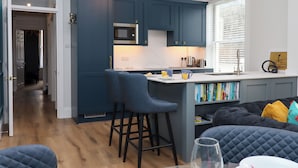 A modern kitchen with dark blue cabinets, a microwave, and a bar area with stools. - Sailors Rest (Dartmouth)