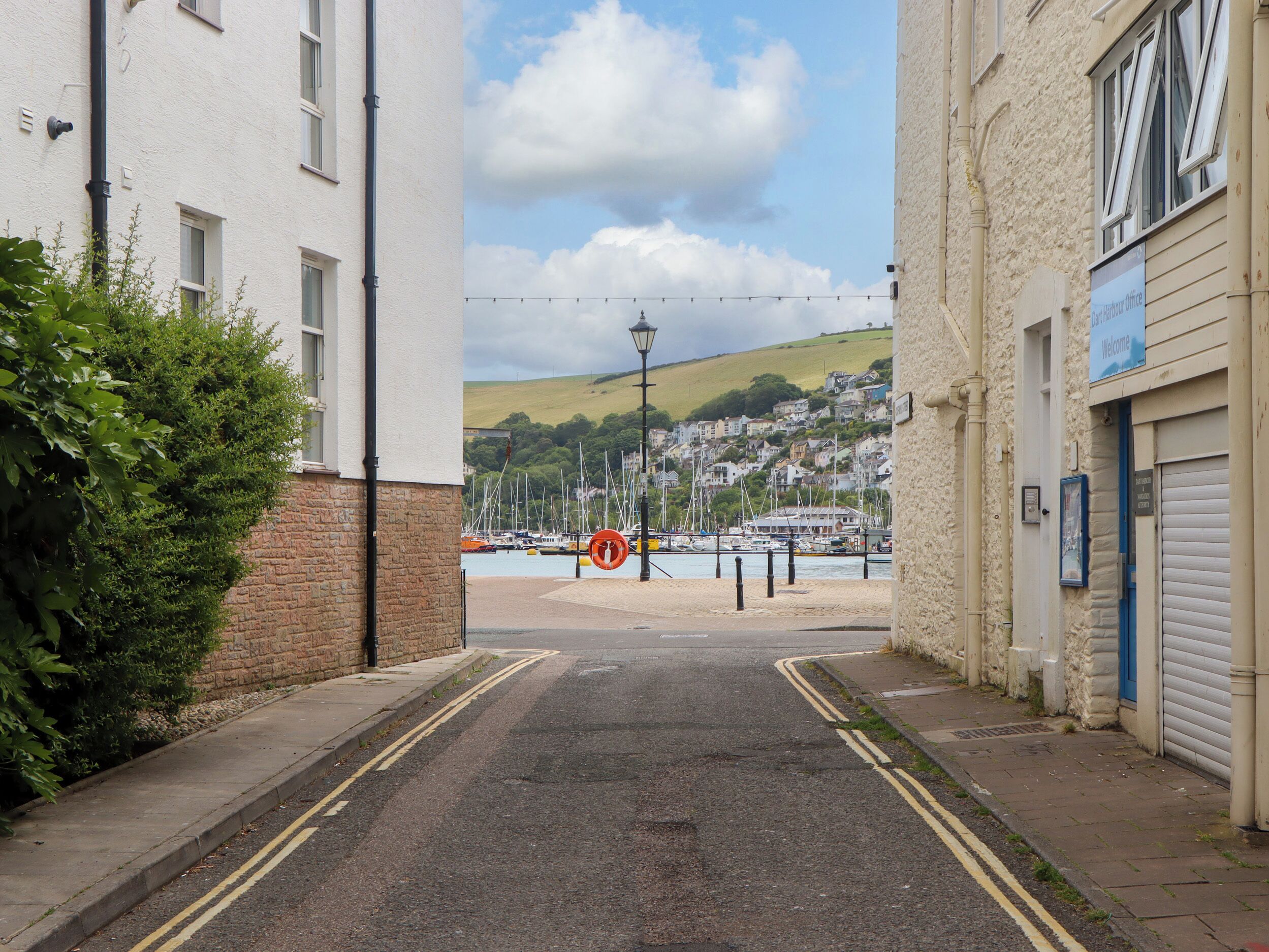 A narrow street leading to a harbor with boats, a 'Welcome' sign, and a 'No Entry' sign.