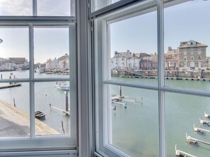 A view through a window of a harbor with boats docked, a pier, and buildings along the water. - Stanley House (Weymouth)