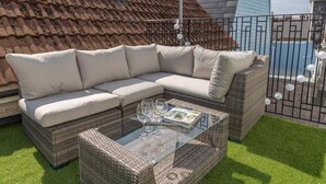 Ein Korbsessel mit Kissen und einem Couchtisch mit Glasplatte, auf künstlichem Rasen platziert.