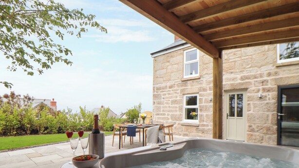 Un bain à remous dans un espace extérieur abrit é, avec des murs en pierre, une table avec des chaises et un jardin en arrière-plan.
