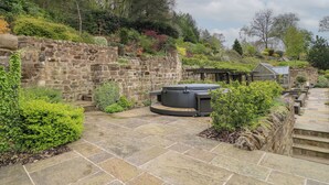 A stone patio with a hot tub, surrounded by lush greenery and a stone wall. - The Barn at Catacol (Belper)