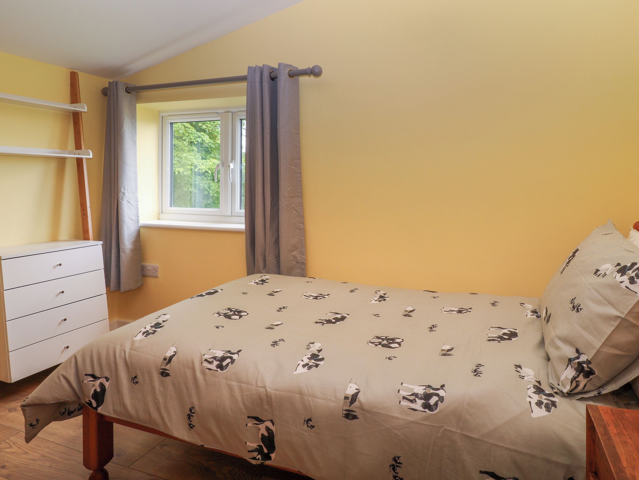 A bedroom with a bed, a dresser, a window with curtains, and a view of greenery outside.