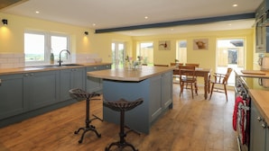 A spacious kitchen with a central island, wooden flooring, and a view of the outdoors. - Muddy Udders Dairy (Okehampton)