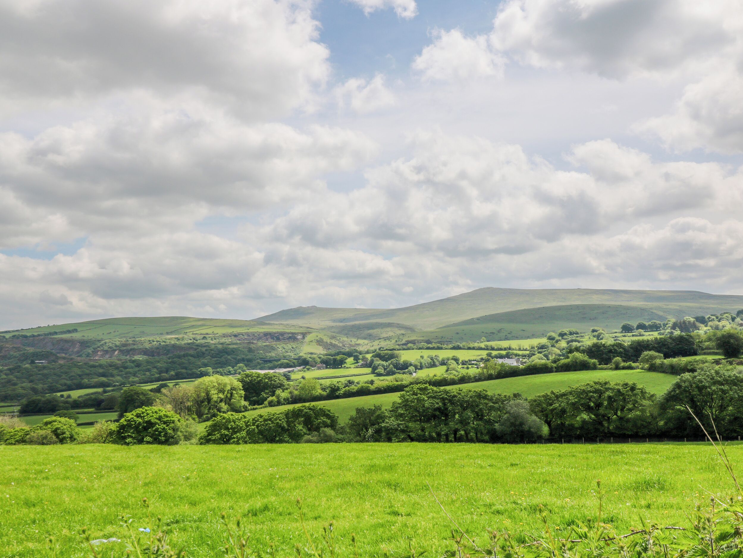 A panoramic view of rolling green hills with a small house nestled among the trees.