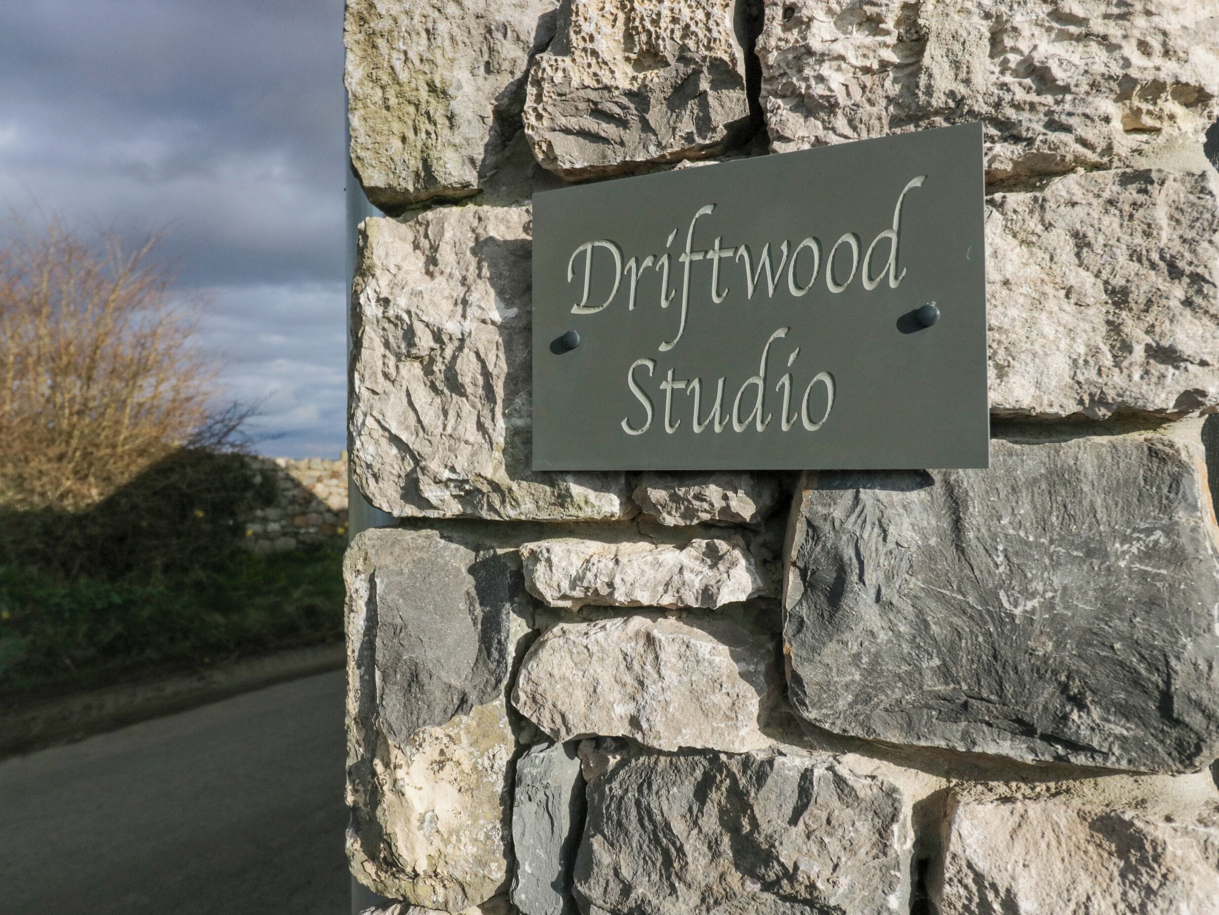 Een stenen muur met een bord waarop 'Driftwood Studio' staat.