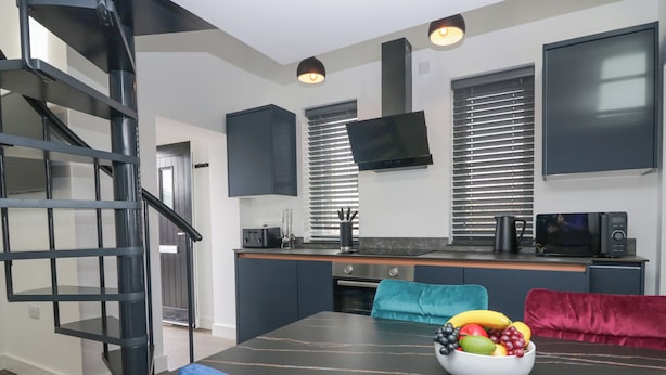 Una cocina moderna con comedor, una escalera espiral negra y un televisor de pantalla plana montado sobre la encimera.