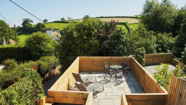 A wooden deck with a table and chairs, surrounded by a garden and a view of the countryside. - The Old Post Office (Dawlish)