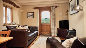 A cozy living room with a brown leather sofa, a wooden coffee table, and a television. - The Old Post Office (Dawlish)