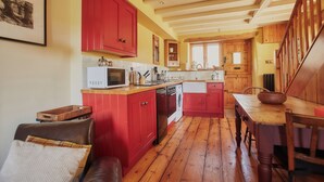 A kitchen with red cabinets, a wooden dining table, and a wooden floor. - The Old Post Office (Dawlish)