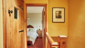 A wooden door leading to a bedroom with a bed, a nightstand, and a framed picture on the wall. - The Old Post Office (Dawlish)